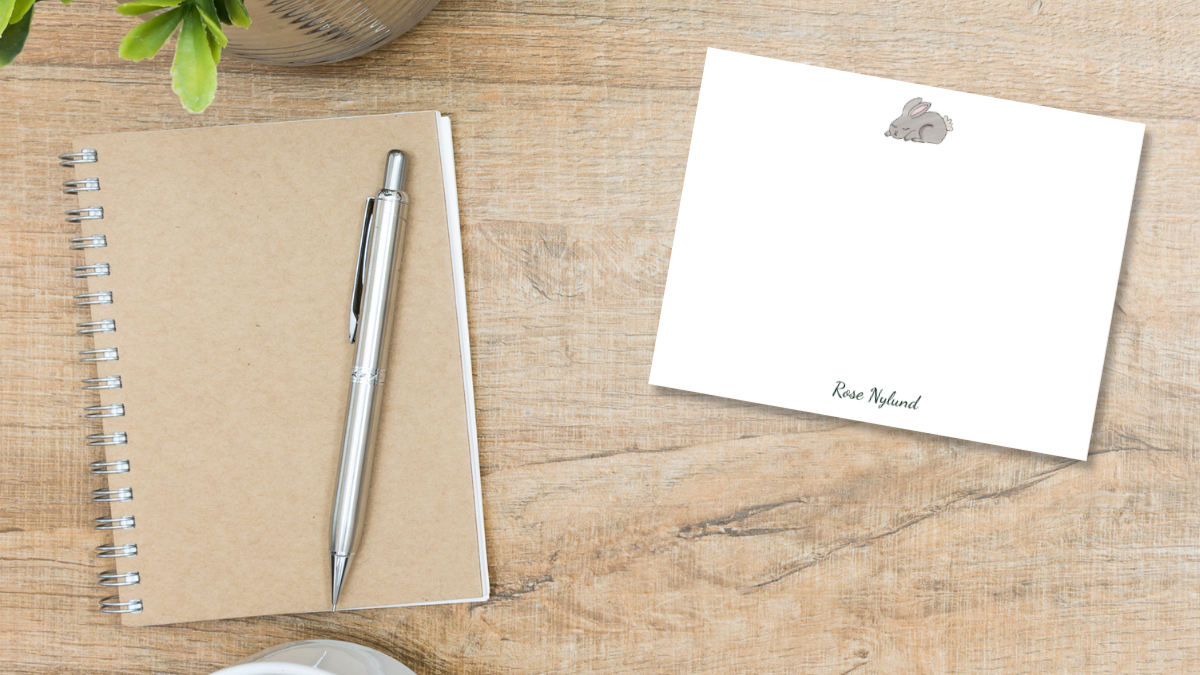 notecard with an illustrated gray bunny and a personalized name laying on a on a desk designed by Viola and Beatrice Stationers