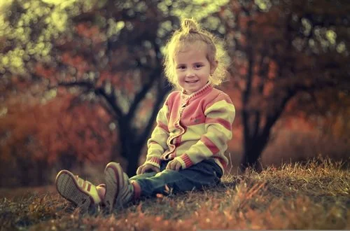 Little girl sitting outside in fall weather with a sweater, smiling
