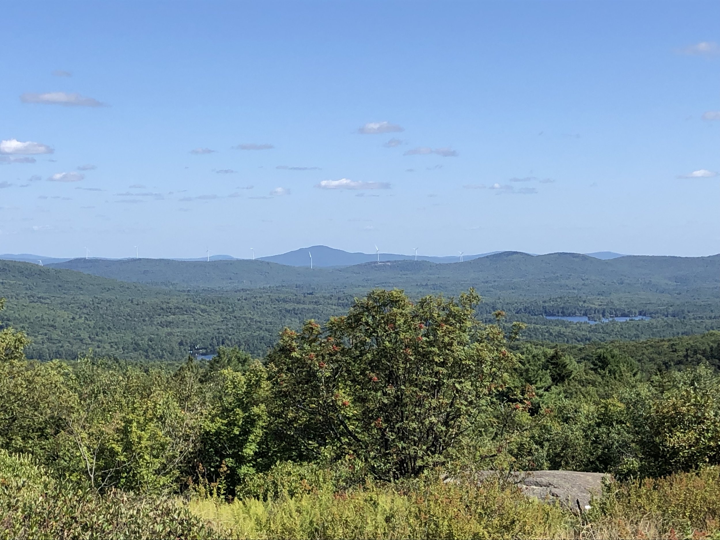 The view from Pitcher Mountain in Stoddard. Island Pond is on the right. The line of new windmills in Antrim is along the ridge in the distance.