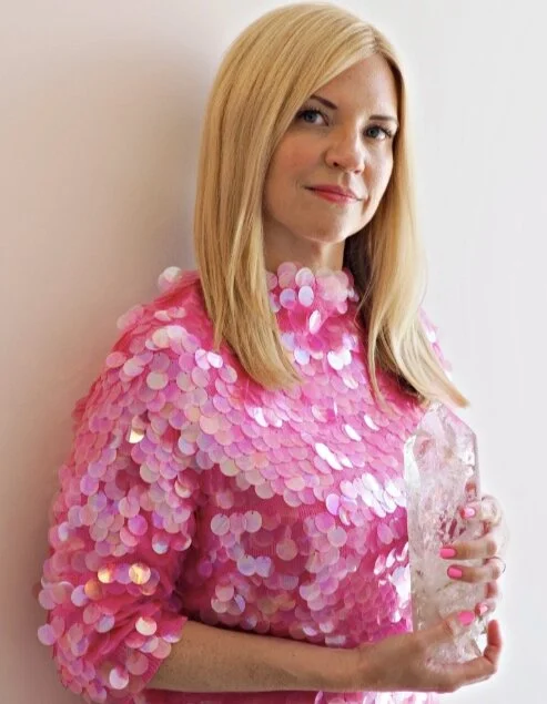 Coleen standing in a pink sequin shirt in the Crystal Cave holding a large clear quartz tower
