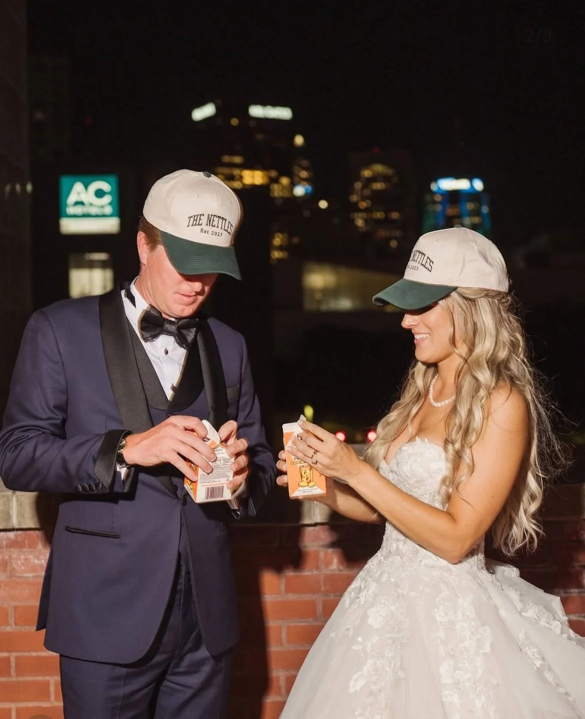 Newly married couple celebrating after their wedding, wearing a lace wedding dress and navy tuxedo with city lights in the background.