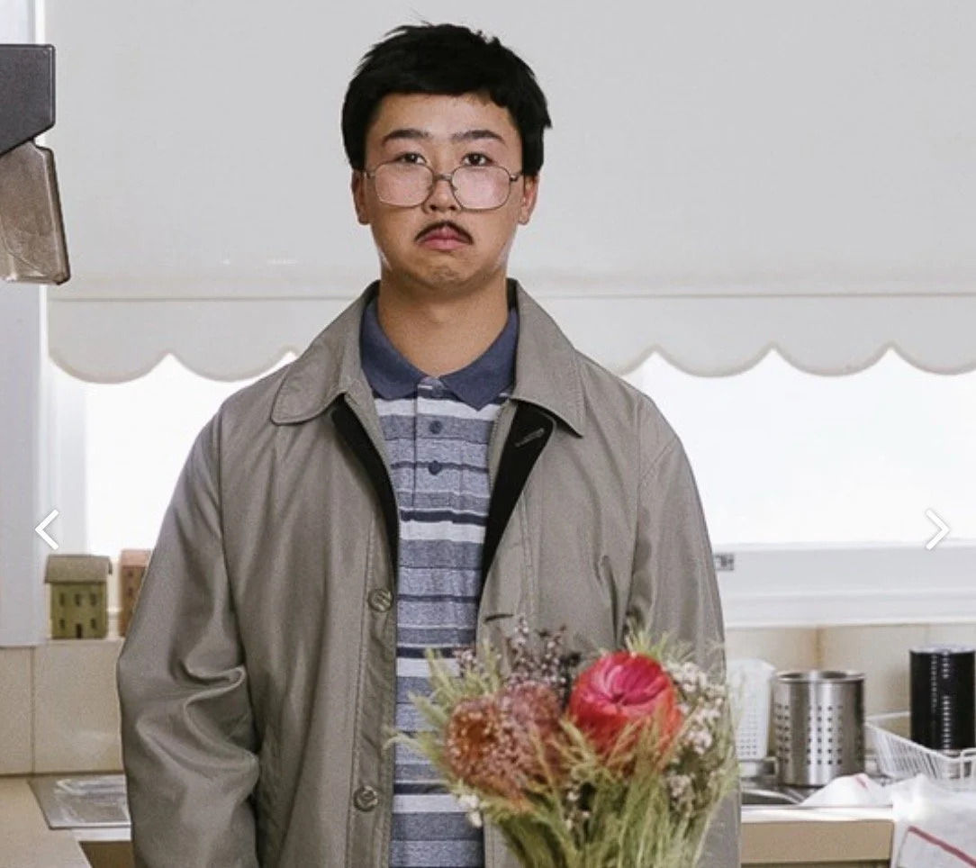 A young man with glasses holding a bouquet of flowers in a kitchen.