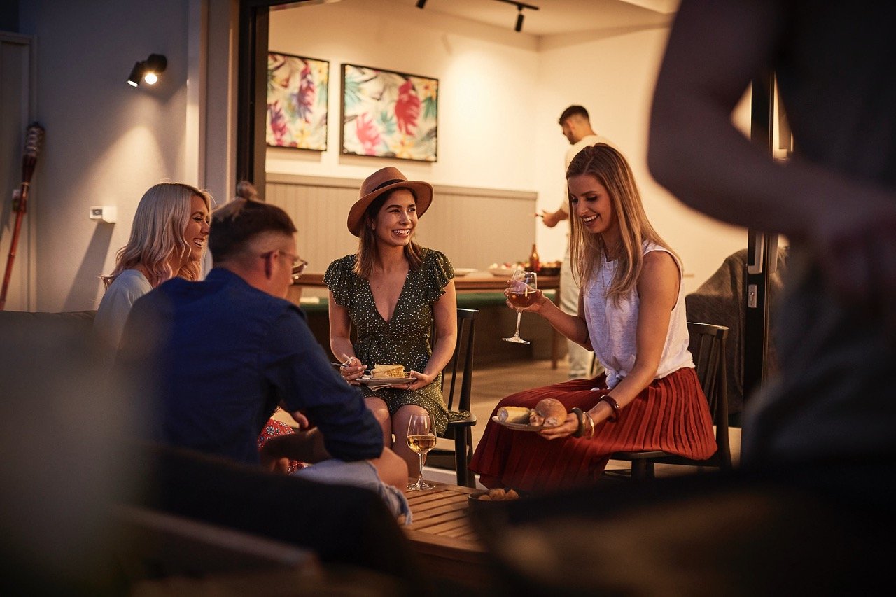 Group of people enjoying drinks and conversation in a cozy indoor setting, with artwork on the wall in the background.