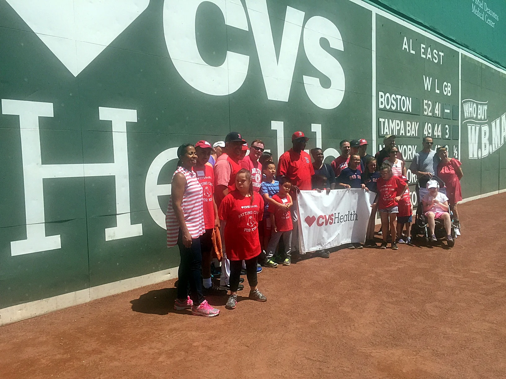 JP Plunkett poses with Milton Little League Challenger players, and Red Sox coaches Chili Davis and Victor Rodriguez in front of Fenway Park's fabled Green Monster. CVS Health sponsored this special event while Red Dome co-sponsors the Milton squad.