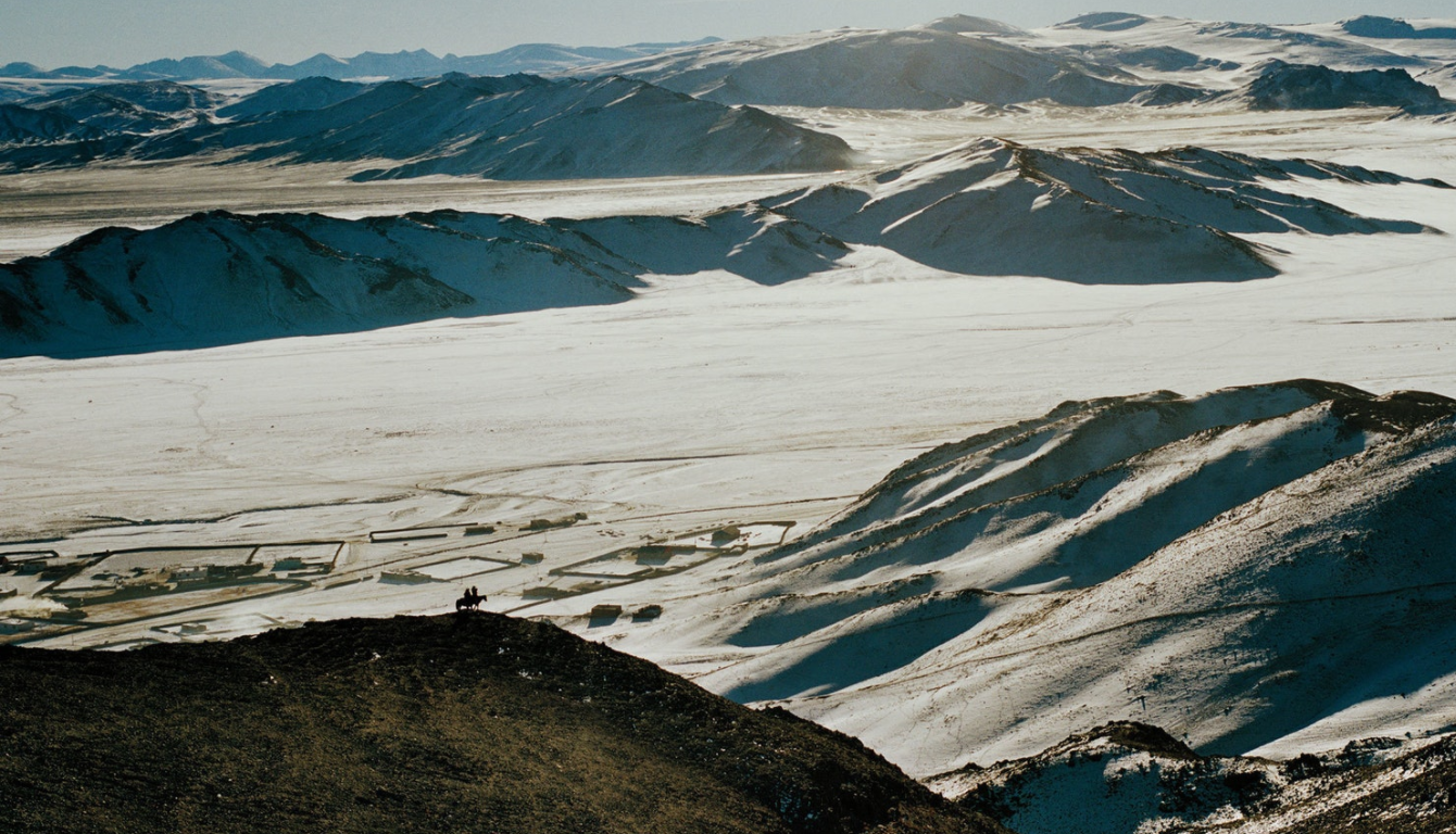 The mountainous landscape dwarfs two Kazakh hunters and their horses in the far west of Mongolia, near the village of Altai (Алтай).