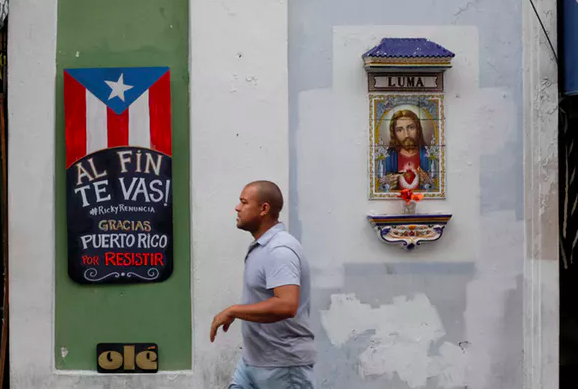 A man walks past a sign that reads ‘You are finally leaving. Ricky resign. Thanks Puerto Rico for resisting’ on the street that leads to La Fortaleza, the official residence of the governor of Puerto Rico. REUTERS/Marco Bello