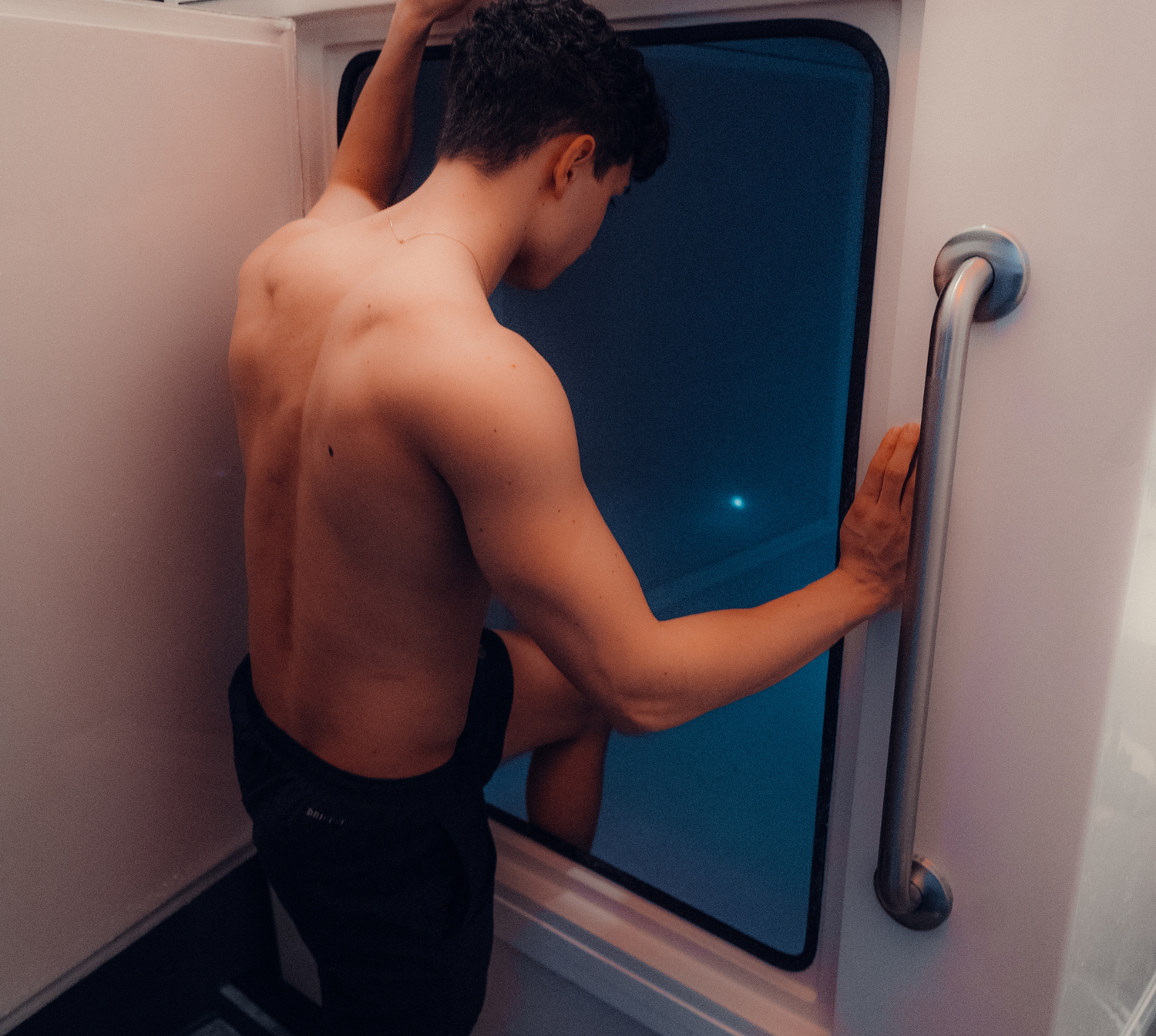 Man in a black swimsuit entering a private float cabin with blue light at Float House Vancouver