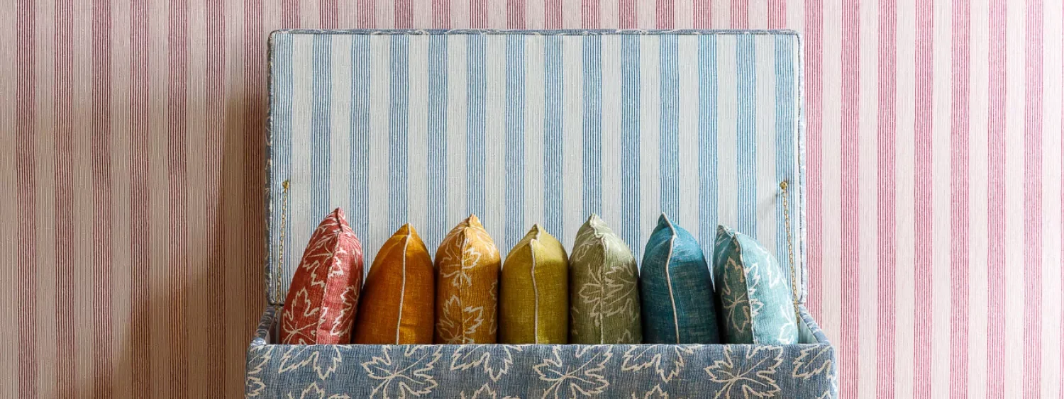 Ticking-stripe-pattern-as-a-background-in-blue-and-pink-with-an-row-of-colourful-cushions-in-maple-pattern.jpg.webp