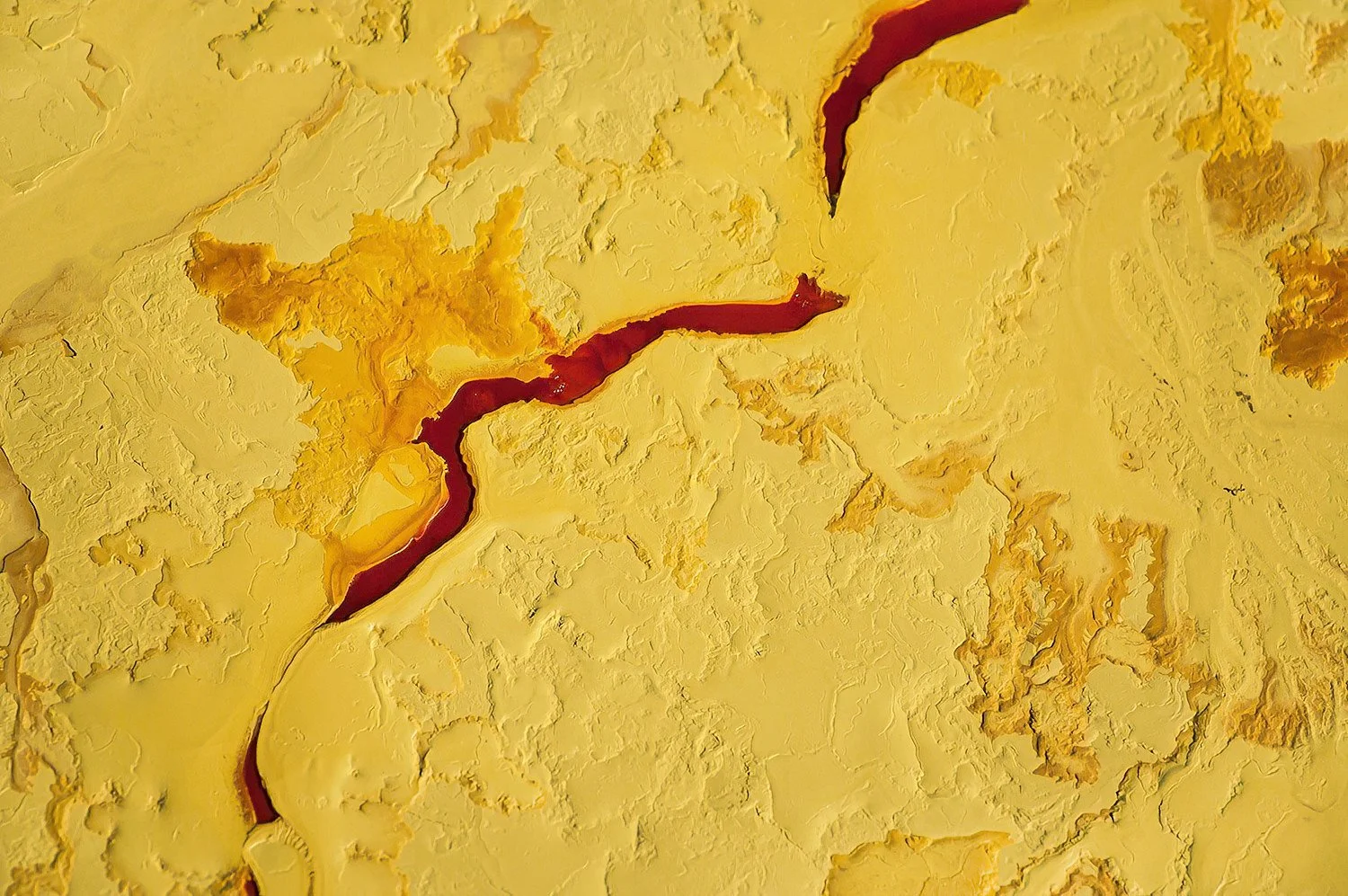 An aerial photo of the Alberta Tar Sands, Alberta, Canada.  Bright yellow sulphur stockpiles contrast with the thick red-brown bitumen extracted from the earth.