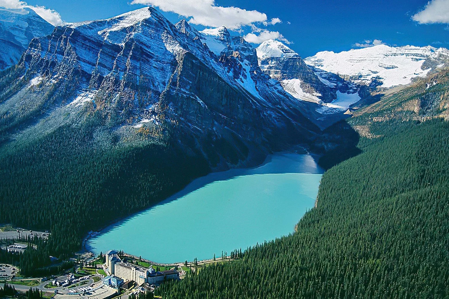 An aerial photo of Lake Louise, Alberta, Canada.  A breathtaking glacial lake renowned for its vivid emerald waters, iconic Fairmont Chateau backdrop, and surrounding snow-capped mountain peaks.