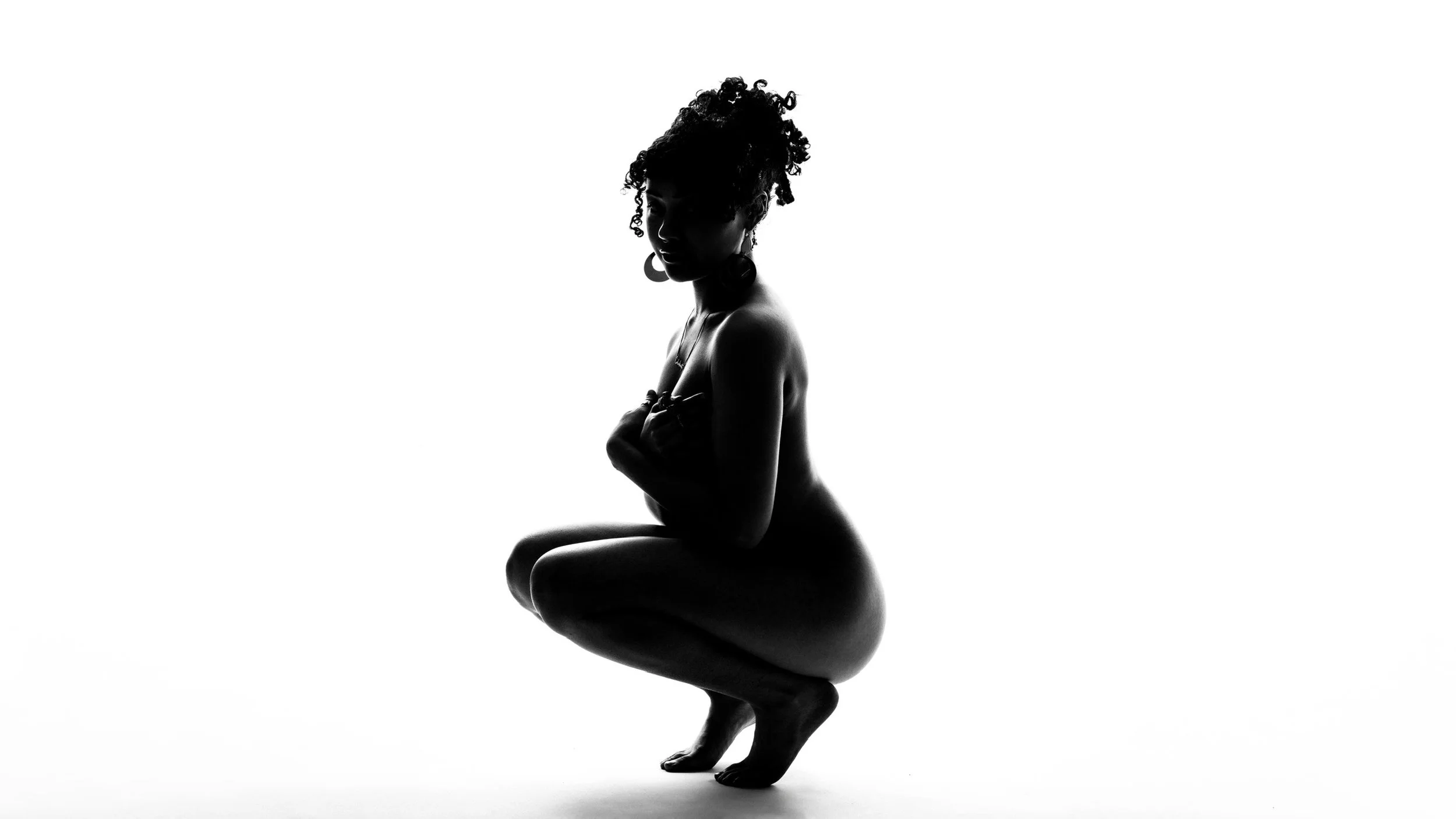 Black and white silhouette of a woman with curly hair in a yoga or dance pose, kneeling with arms crossed over her chest and head turned slightly.