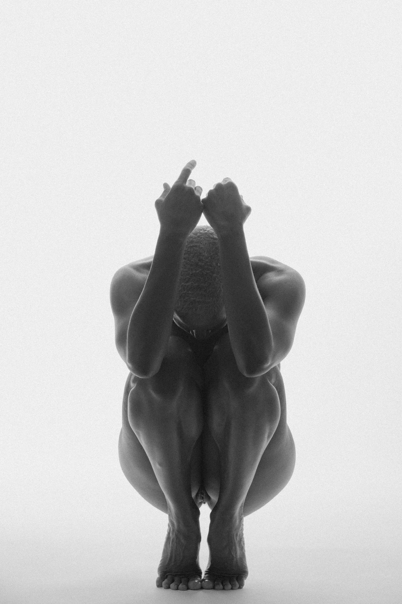 Black and white sculpture of an abstract human figure with exaggerated muscles, holding a finger to its lips in a shushing gesture, standing on a base.