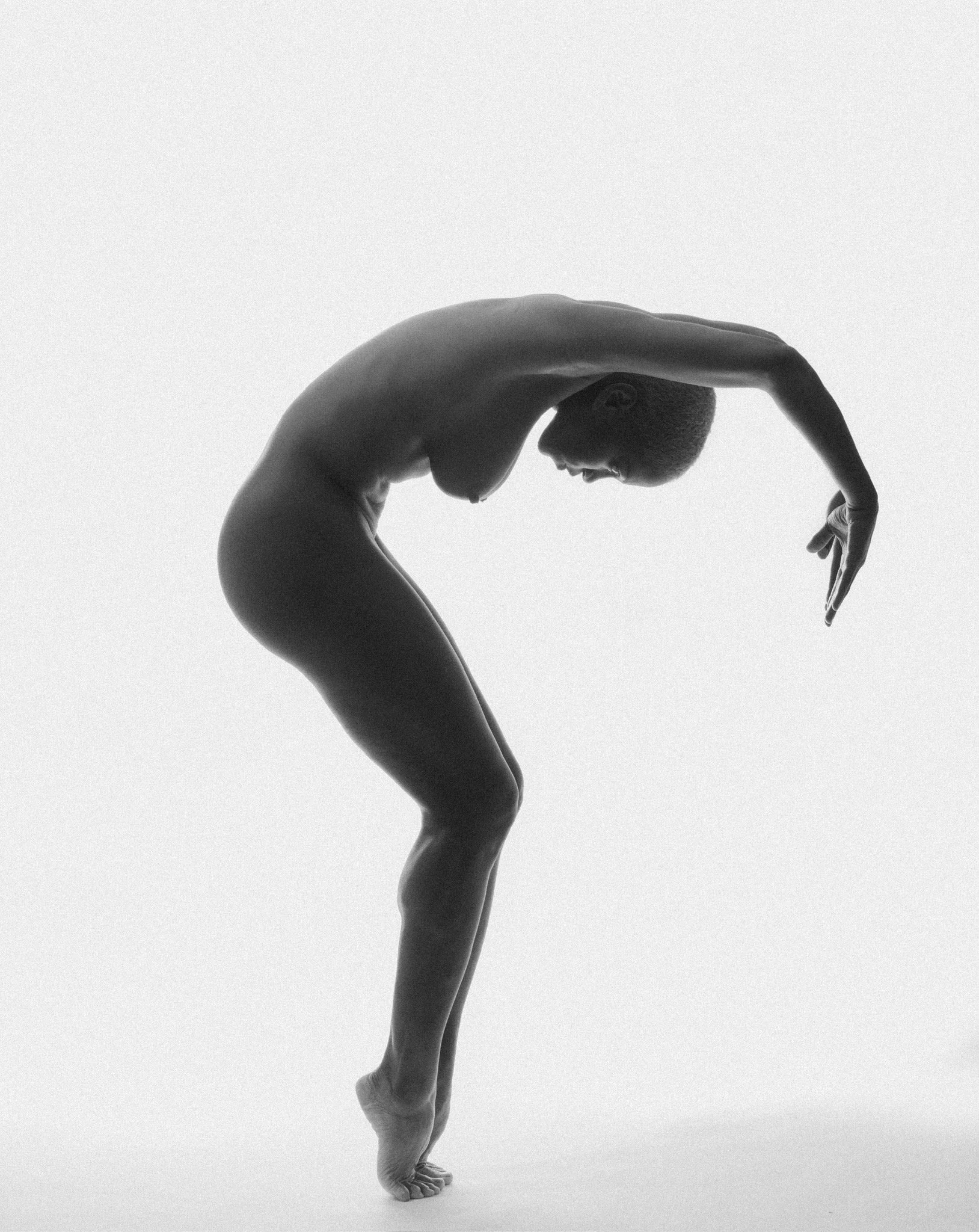Black and white photo of a person doing a handstand with their body curved in a circle, head near their legs, arms extended downward.