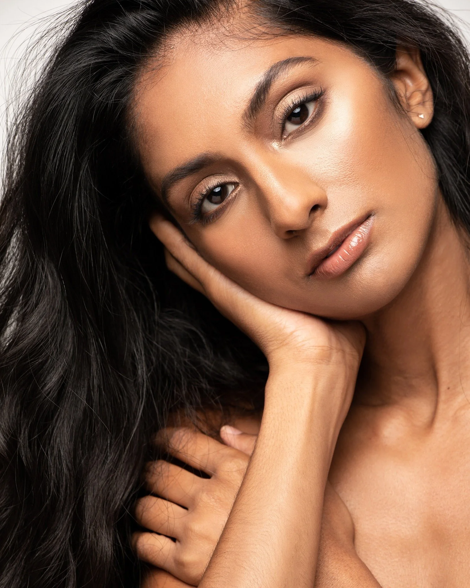 Close-up of a woman with dark hair, resting her face in her hand, showing her face and shoulder.