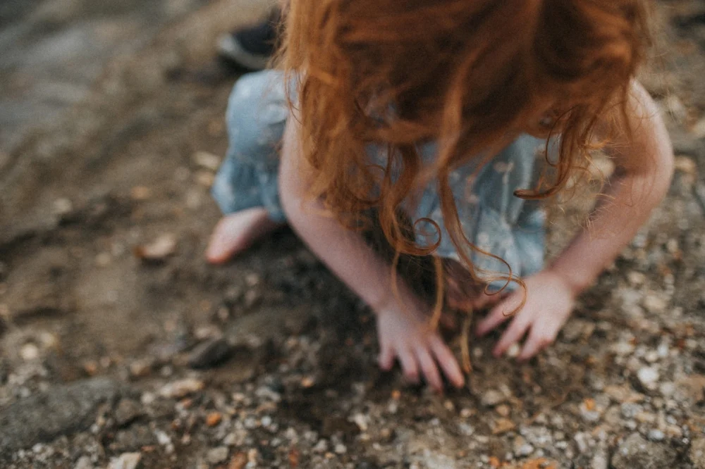 little girl playing in sand on the beach, red hair curls