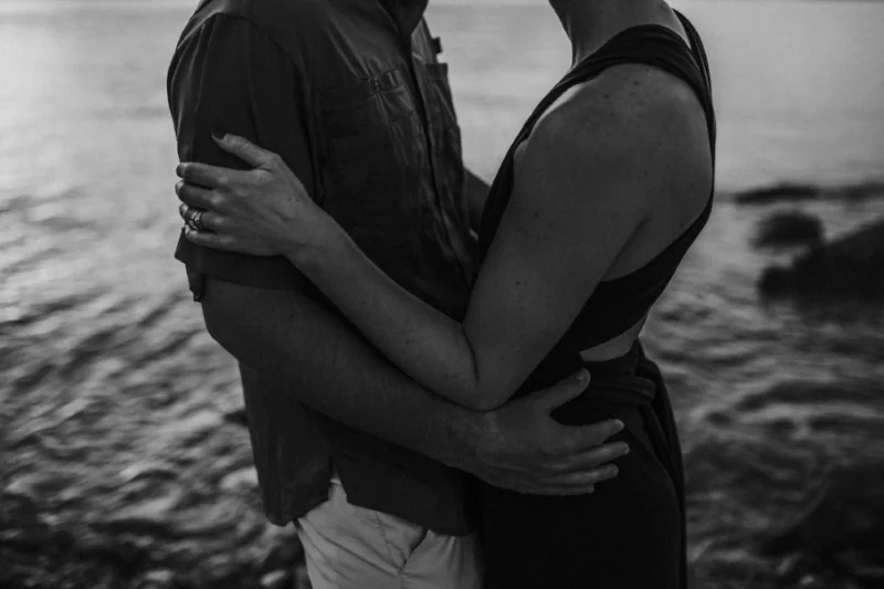 romantic couple embracing by rocky water in black and white