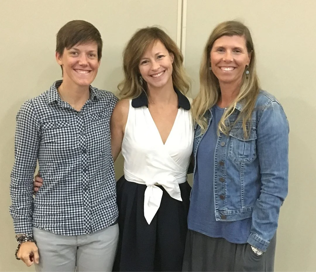 Photo: L to R, Jessica Dallman (wearing a blue and white checkered button-down shirt and grey pants), Elizabeth Seeliger (wearing a dress with a white top and black skirt), and Leigh Hardin (wearing a grey skirt, blue blouse, and jean jacket).