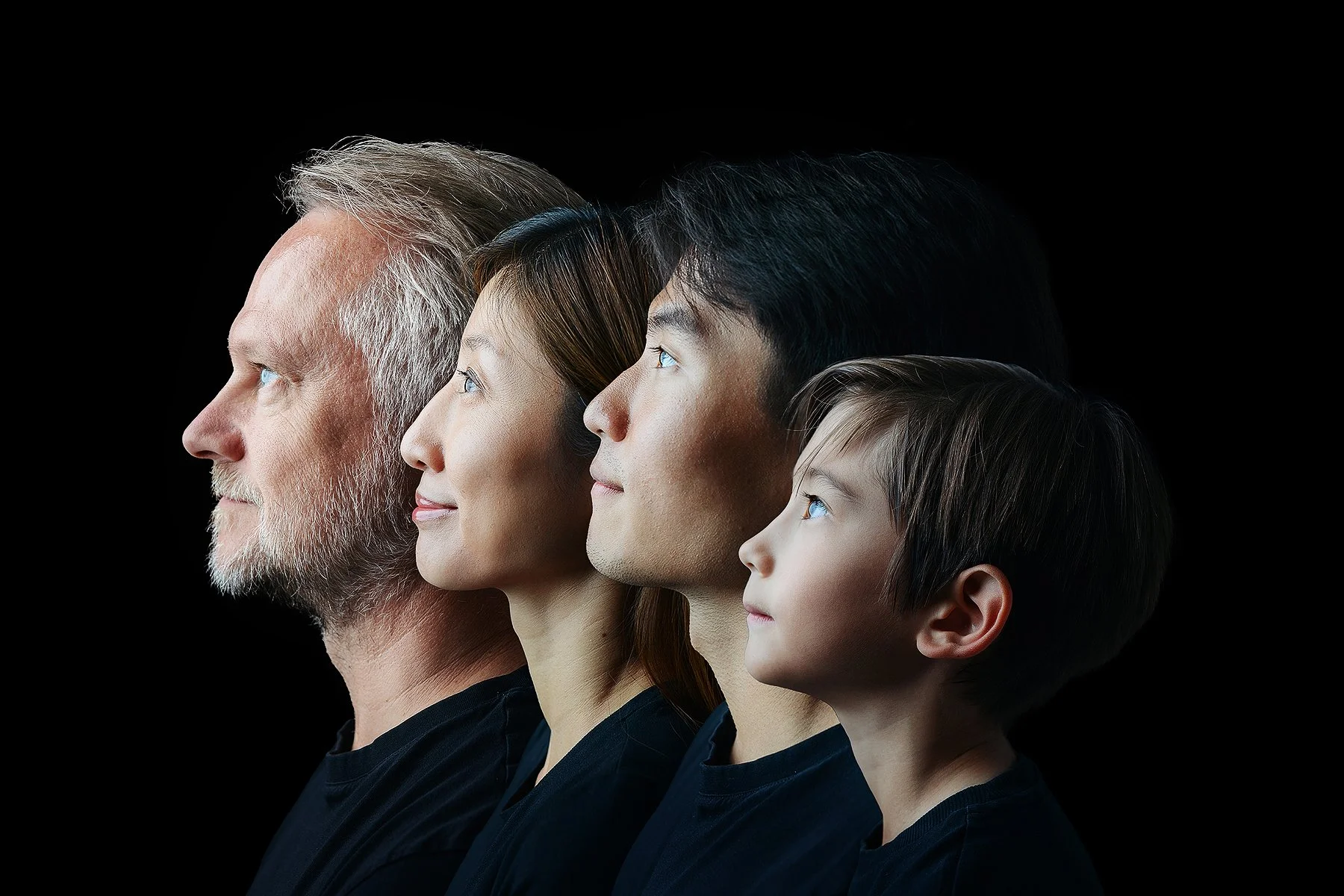 Profile view of four people of different ages, from young child to elderly man, looking upwards against a black background. Generation Portrait Photo by Lenka Wills Photography, Bath UK