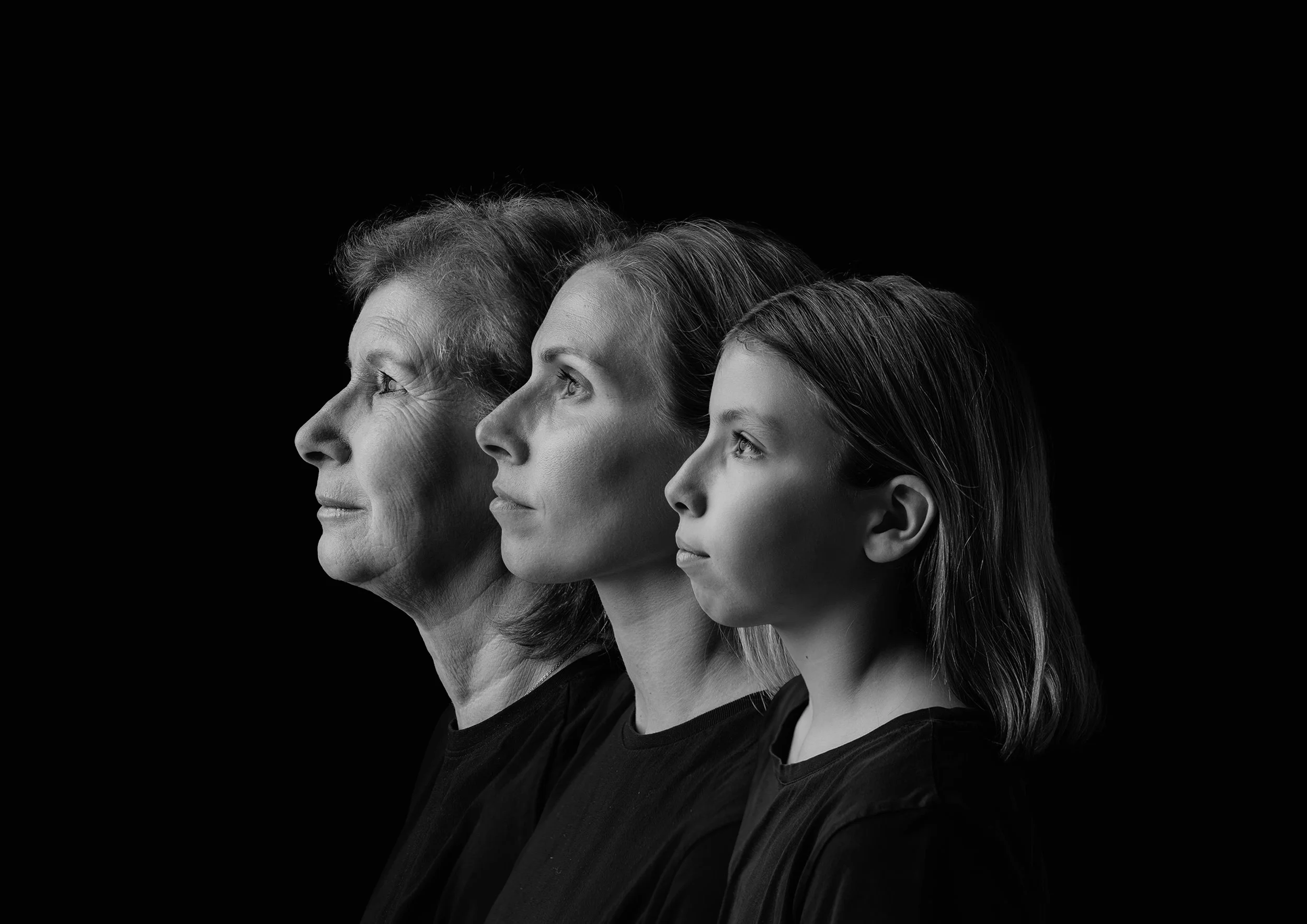 Profile photo of three generations from elderly to young, in black and white, looking to the right against a black background. Photo by Lenka Wills Photography, Bath UK