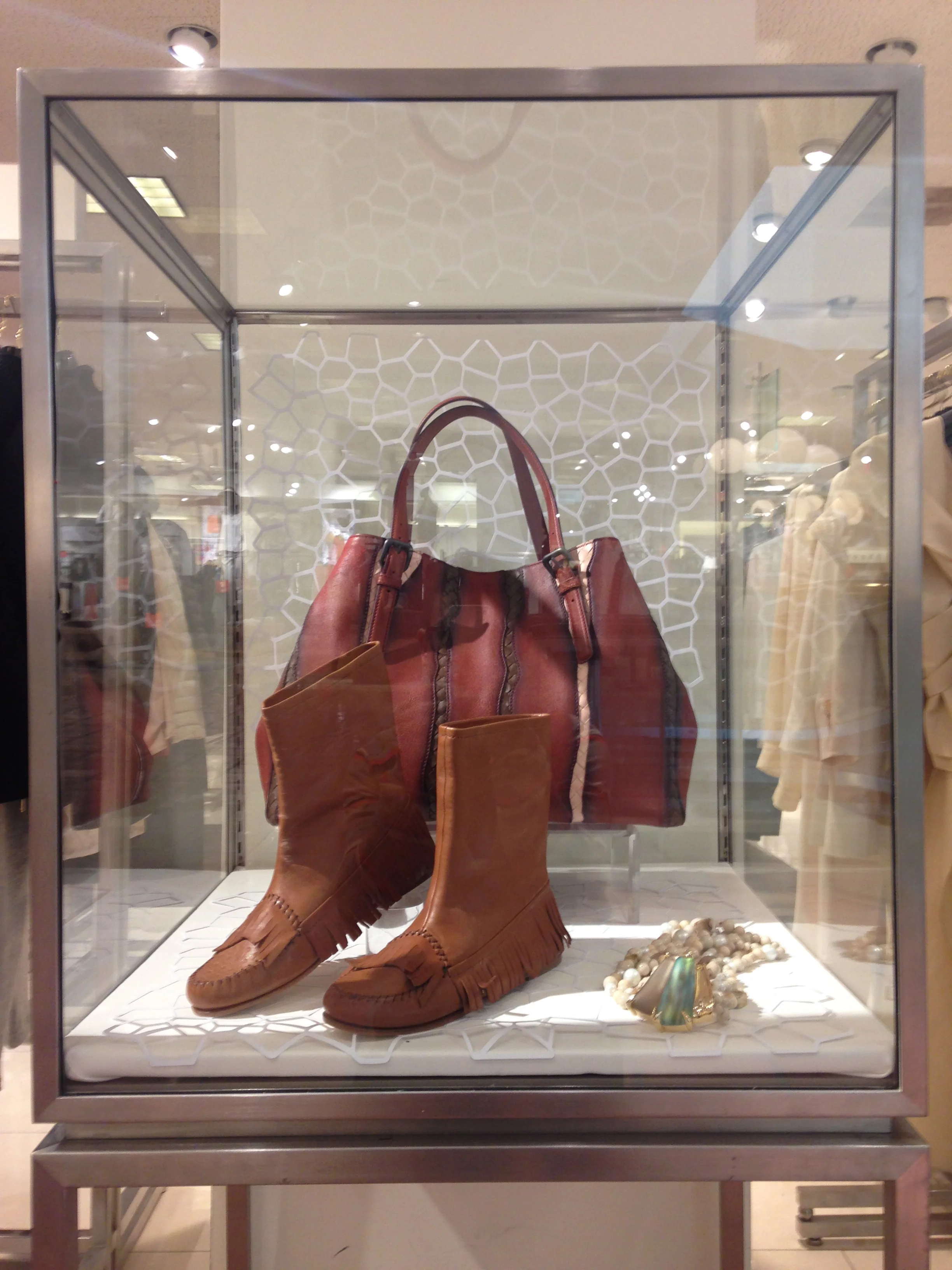 Display case containing brown fringed leather shoes, a matching leather handbag, and jewelry including a pearl necklace and a turquoise stone bracelet.