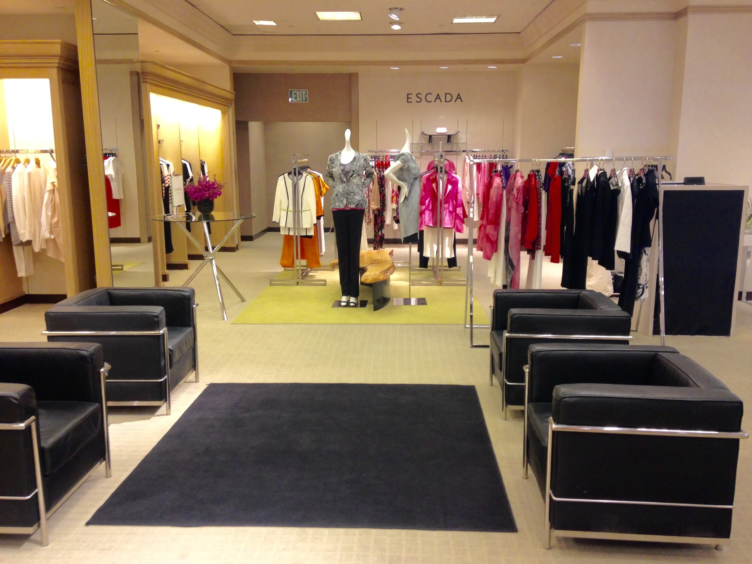A clothing store display with mannequins dressed in fashionable outfits, racks of clothes, and a sign that says 'ESCADA' in the background.