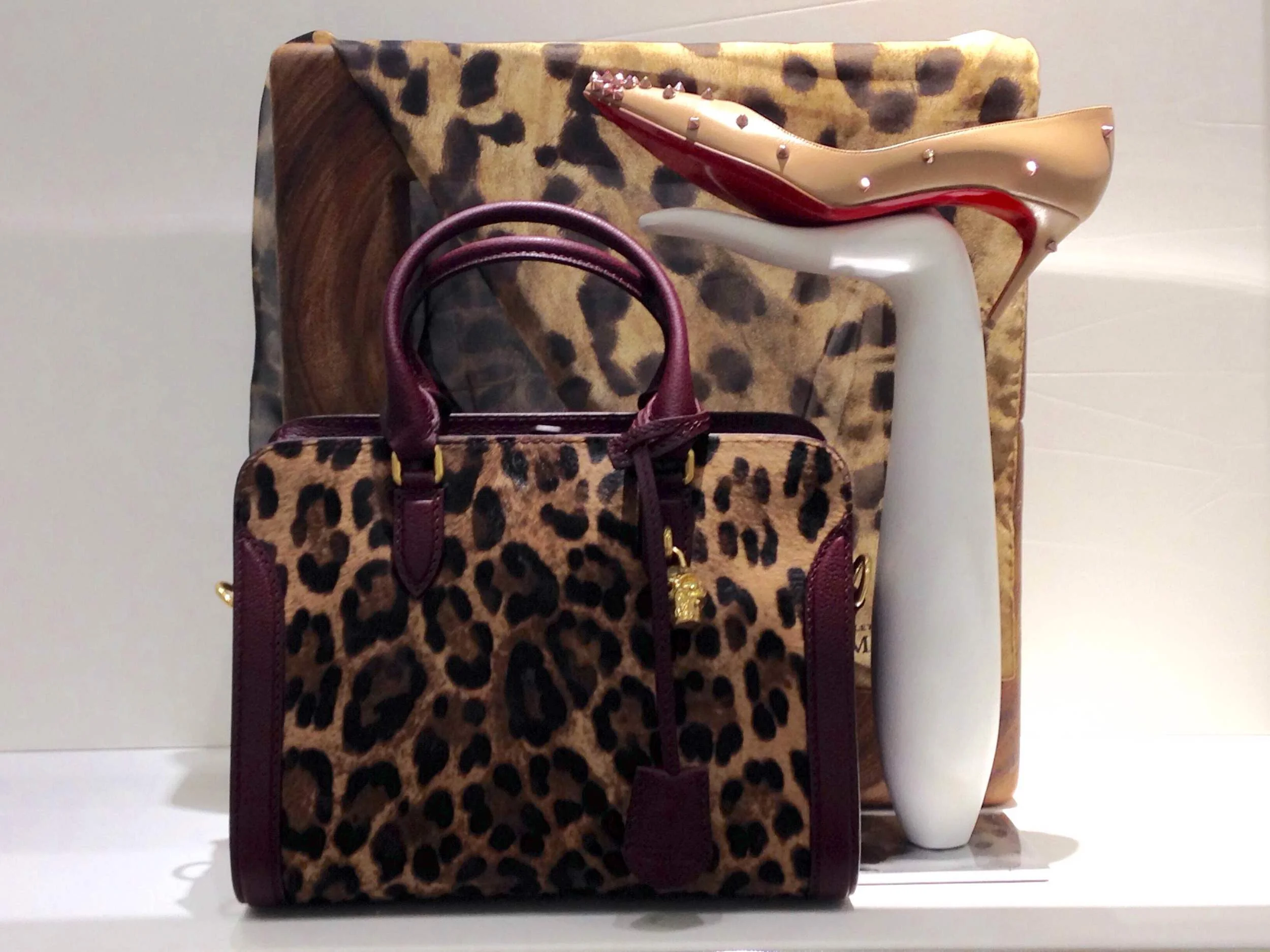 A leopard print handbag placed on a white surface with a leopard print chair in the background and a white decorative object to the right.