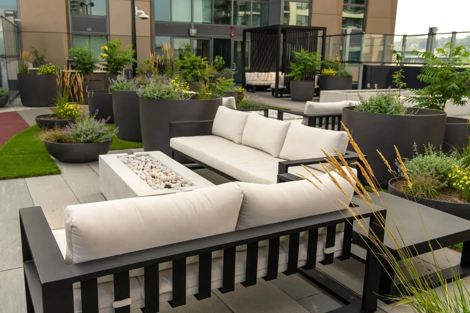 Contemporary outdoor lounge area featuring aluminum-frame sofas with white cushions and a concrete fire table on a urban luxury condominium rooftop deck.