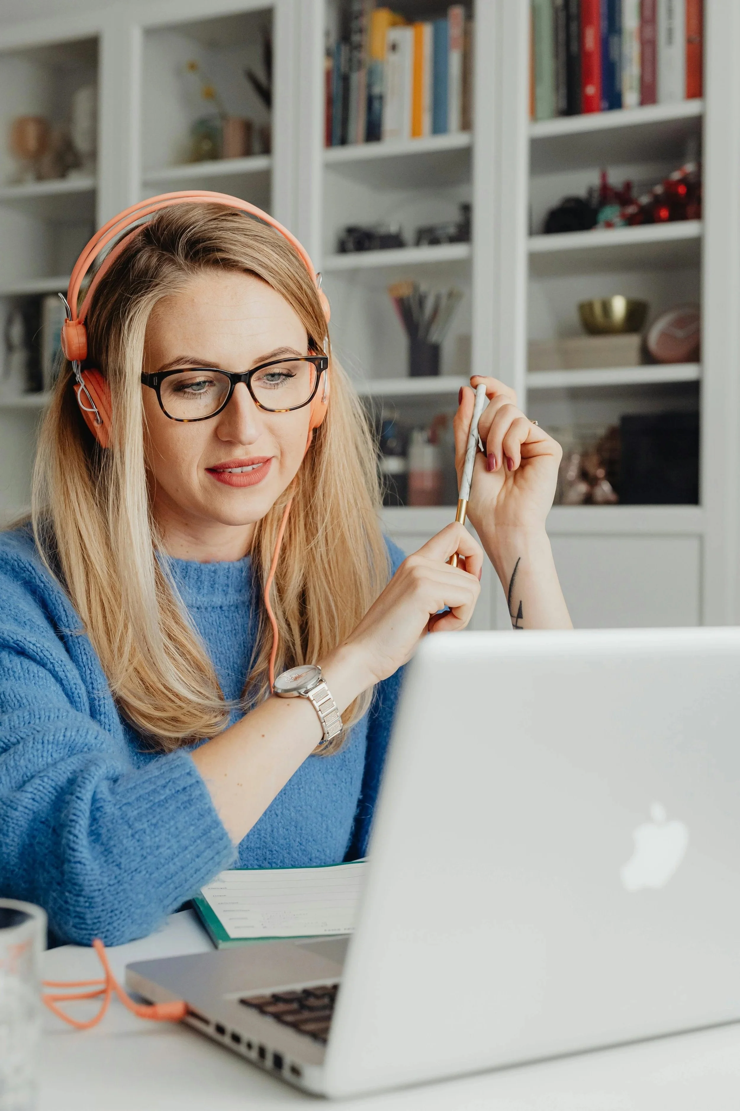 A woman with blonde hair, working at a desk with a silver laptop.