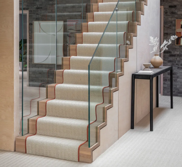 Interior staircase with beige carpet, glass railing, wooden side panels