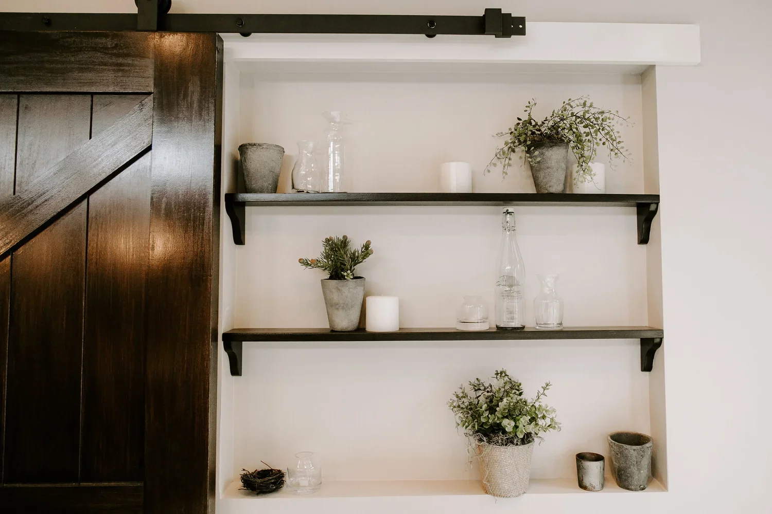 Built-in wall niche with floating dark wood shelves, a contrasting white surround, and a dark wood sliding barn door.
