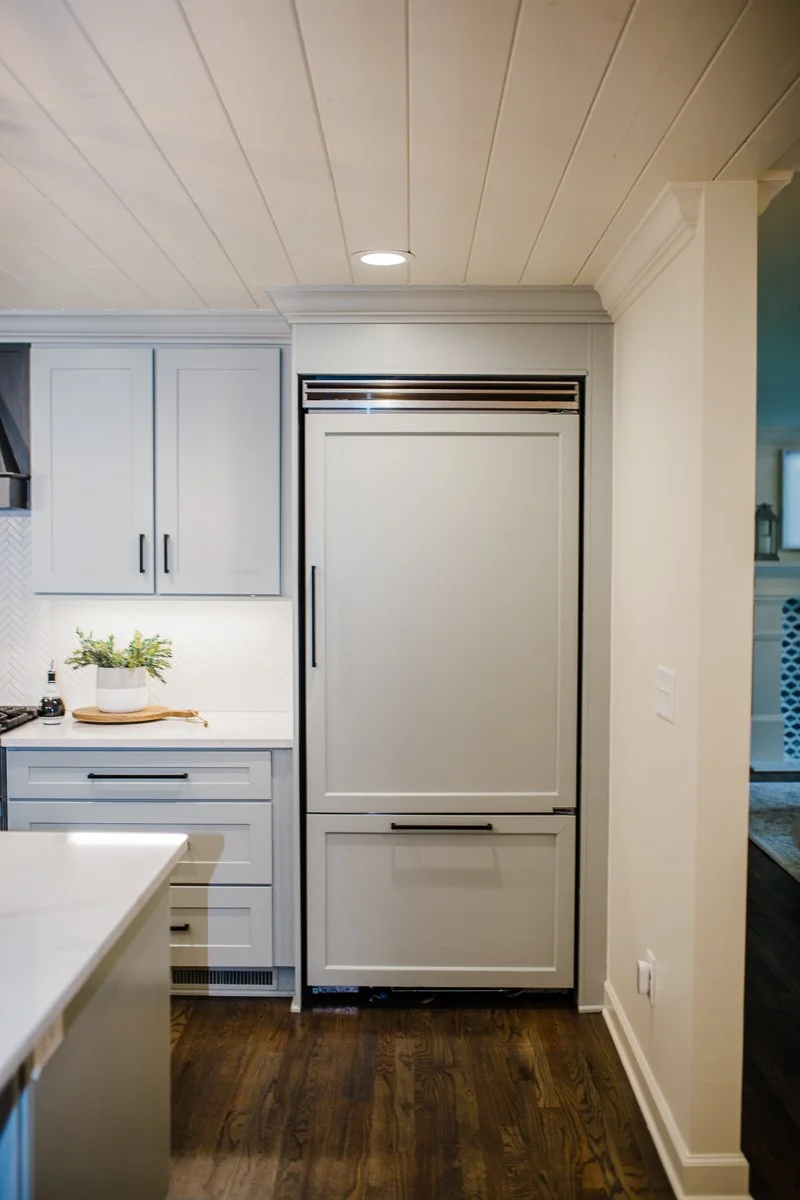 Contemporary kitchen with a panel-ready built-in refrigerator, ceiling-height white shaker cabinetry, white quartz island, subtle herringbone tile backsplash, and dark stained hardwood flooring.
