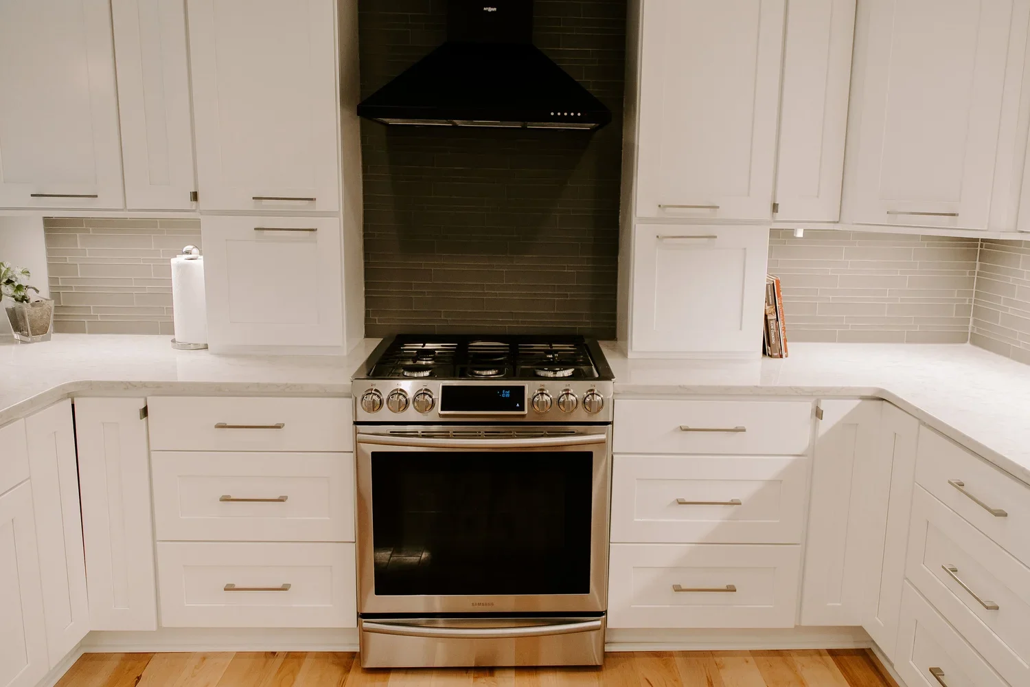 Kitchen with white cabinets, a stainless steel oven, a black range hood, and a gray backsplash.