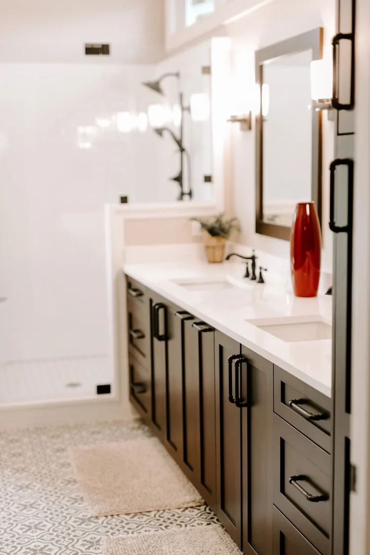 Modern bathroom with a double-sink vanity featuring dark shaker-style cabinetry, bright white quartz countertops, matte black hardware and faucets, black-framed mirrors with wall sconces, a frameless glass walk-in shower, and black-and-white patterne