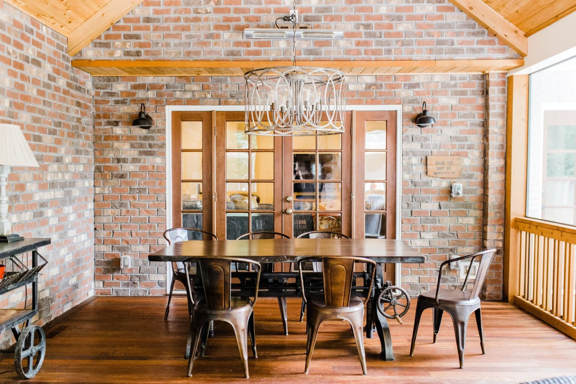 Covered dining porch with exposed brick walls, vaulted wood beam ceiling, French doors, and warm wood flooring.
