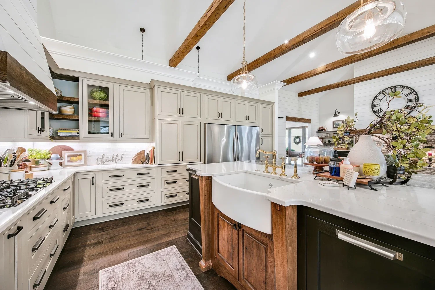 Modern farmhouse kitchen with white cabinets, a large kitchen island with a farmhouse sink, and exposed wooden ceiling beams.
