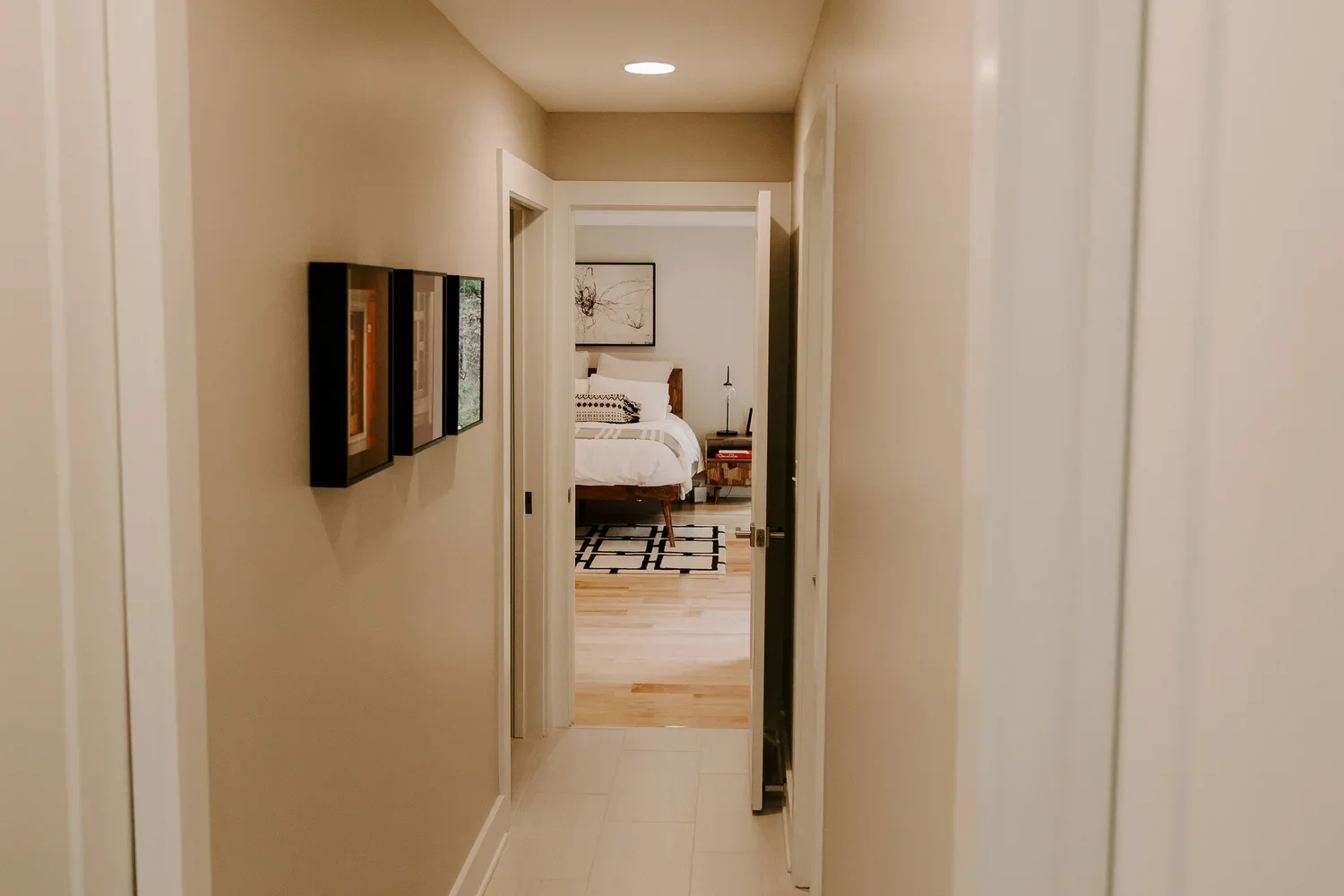 View down a hallway leading to a bedroom with a bed, a nightstand, and artwork above the headboard.