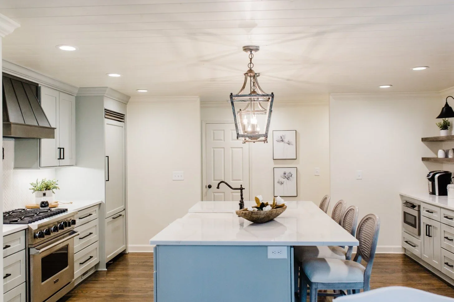Modern kitchen with white cabinets, stainless steel appliances, a large white island with seating, pendant lighting, and decorative wall art.