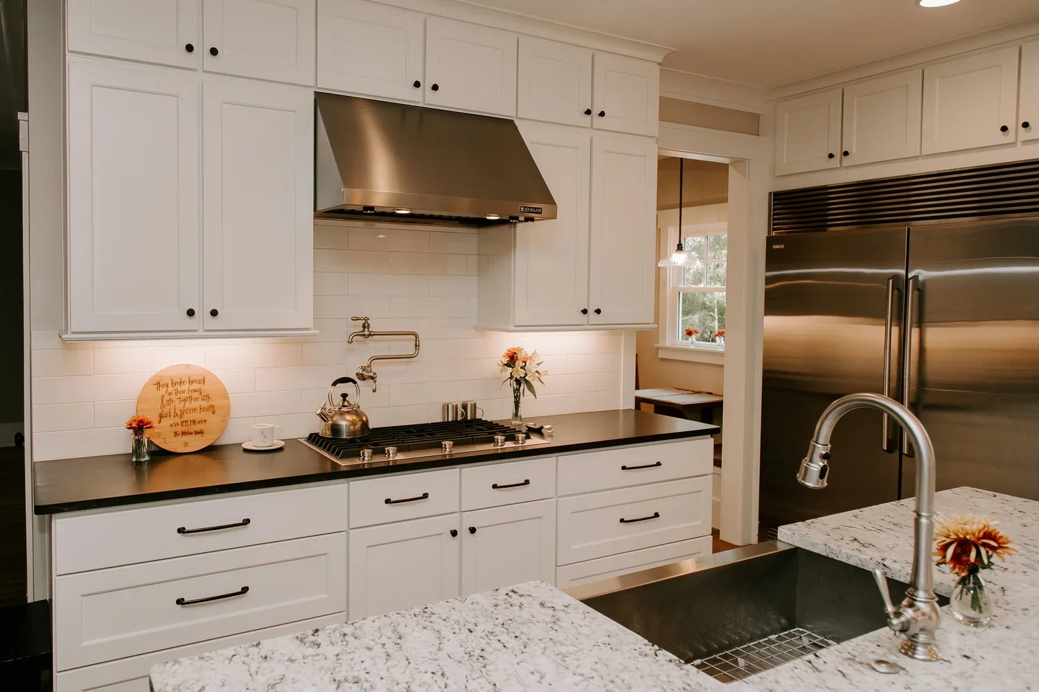 Contemporary kitchen with ceiling-height white shaker cabinetry, a large white-and-gray veined quartz island with an undermount stainless steel sink and gooseneck faucet, professional-grade stainless steel refrigerator, white subway tile backsplash w