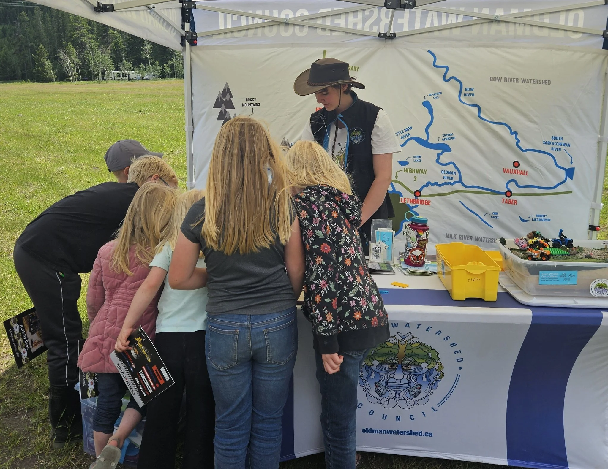 a woman at an outdoor booth talking to a group of kids