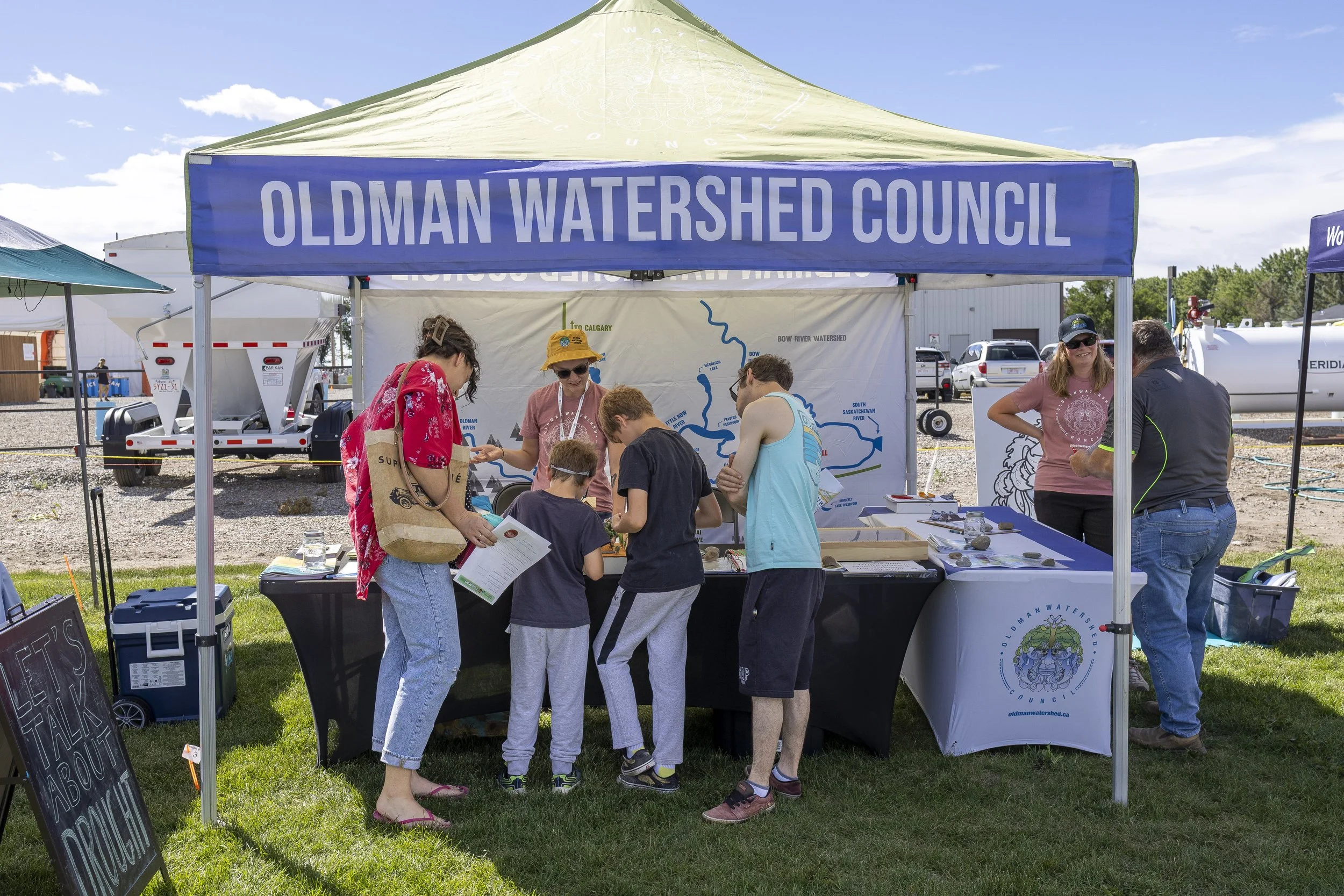 a family speaks to two OWC employers, wearing pink shirts, at a booth set up in a field