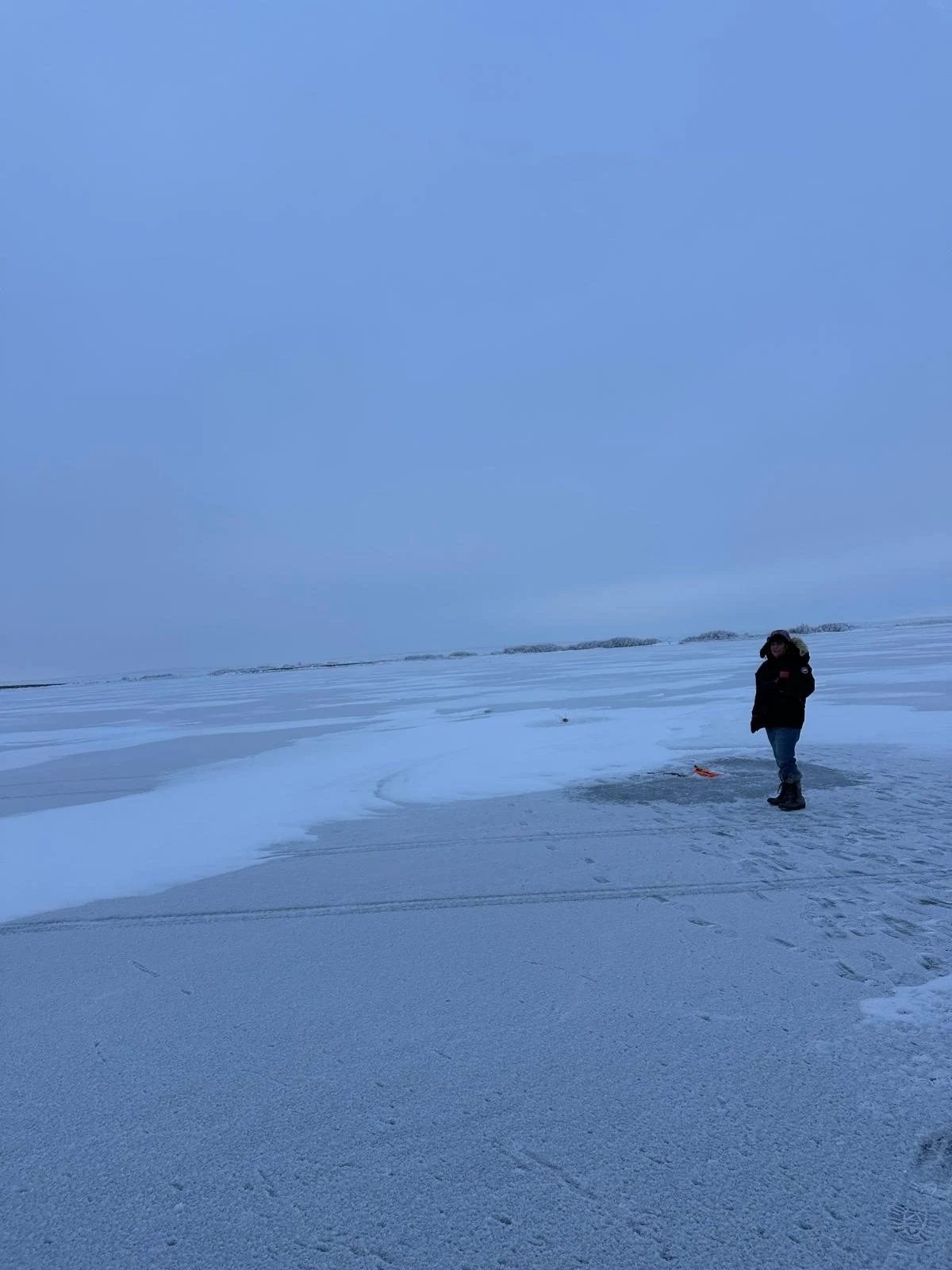a woman standing on an icy body of water near a fishing hole