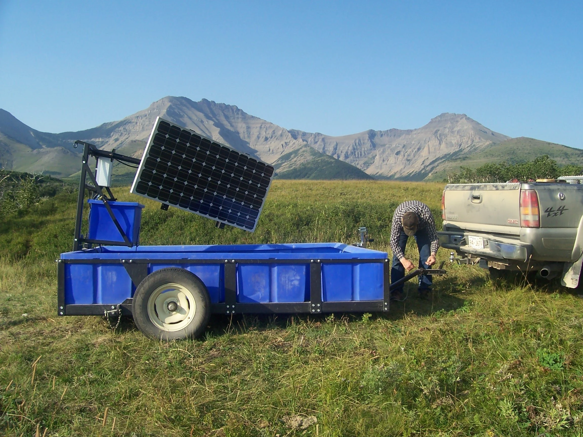 a rancher unhooks a blue tub with a solar panel overhead from the back of a truck