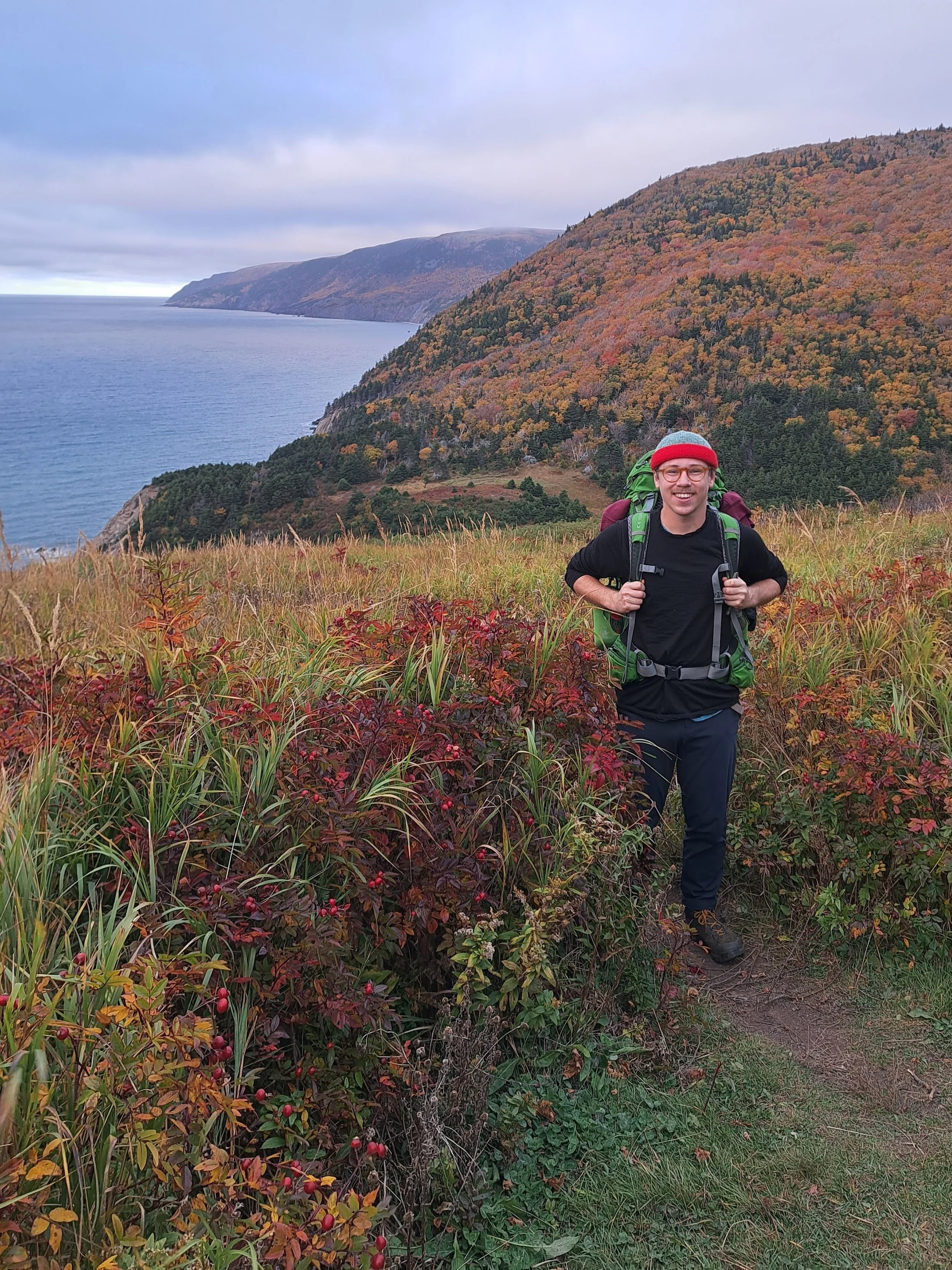 Elijah, wearing a backpack and toque, on a coastal hike in the fall