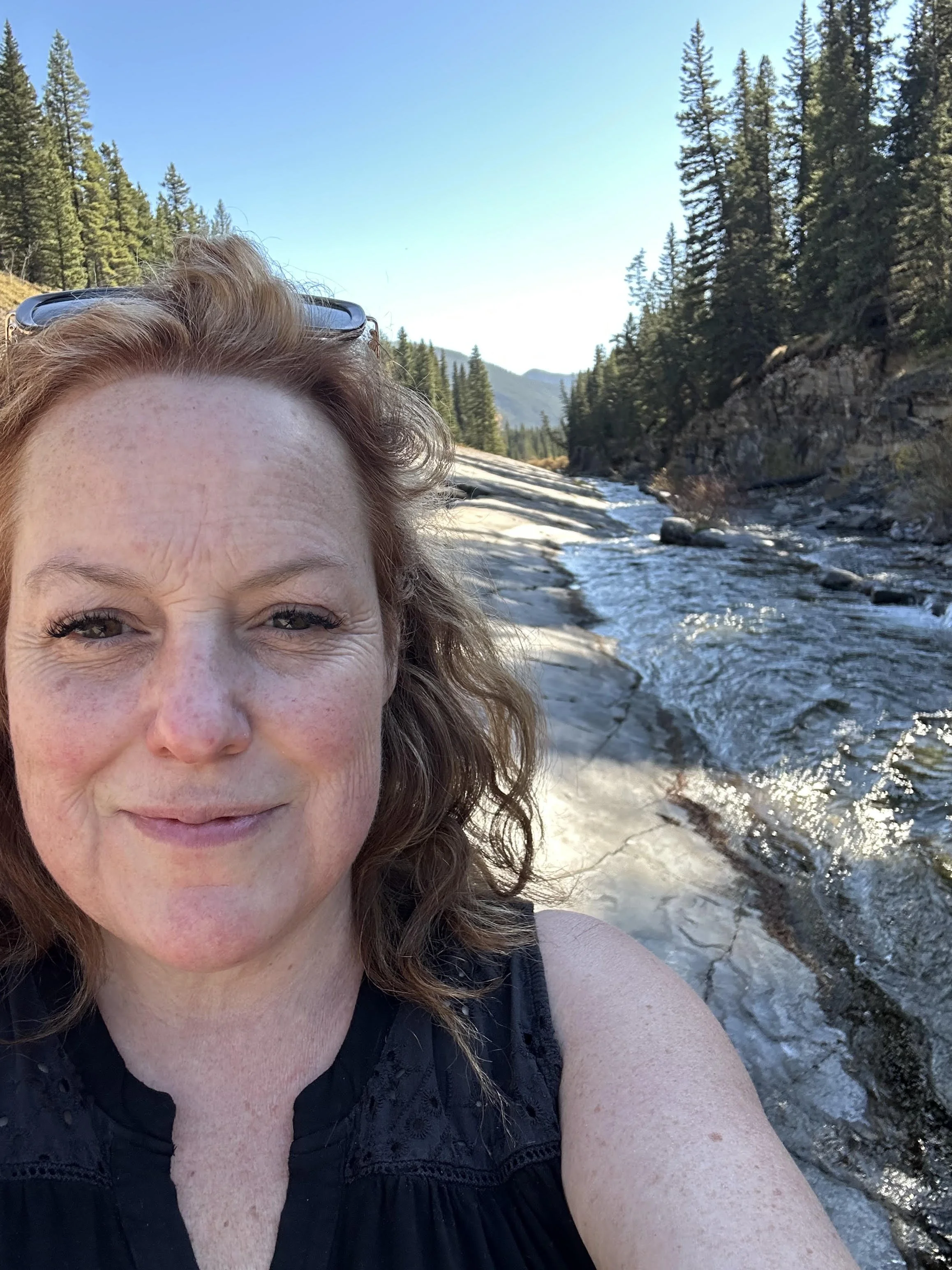 a selfie of Angela with a tree-lined river in the background