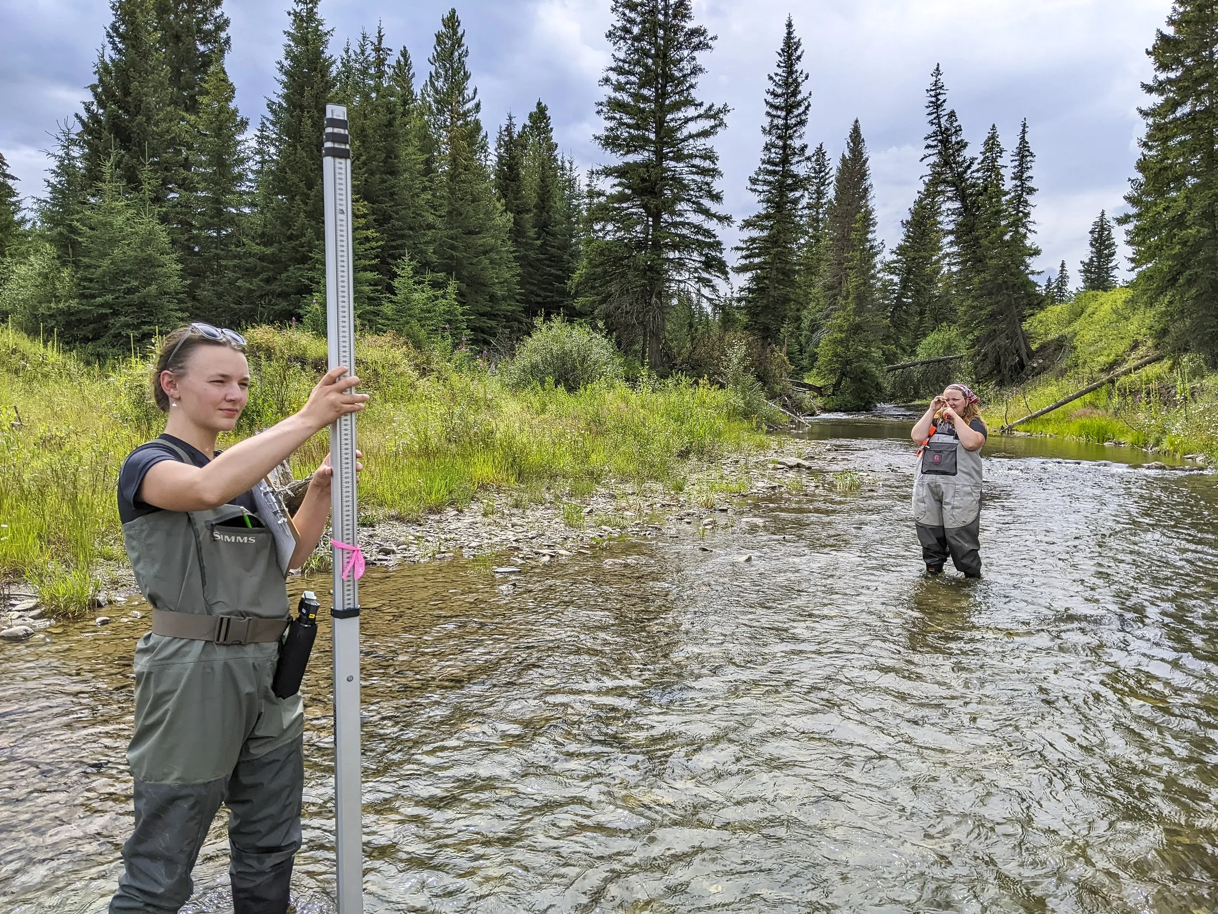 two people wearing hip waders standing in a creek taking measurements