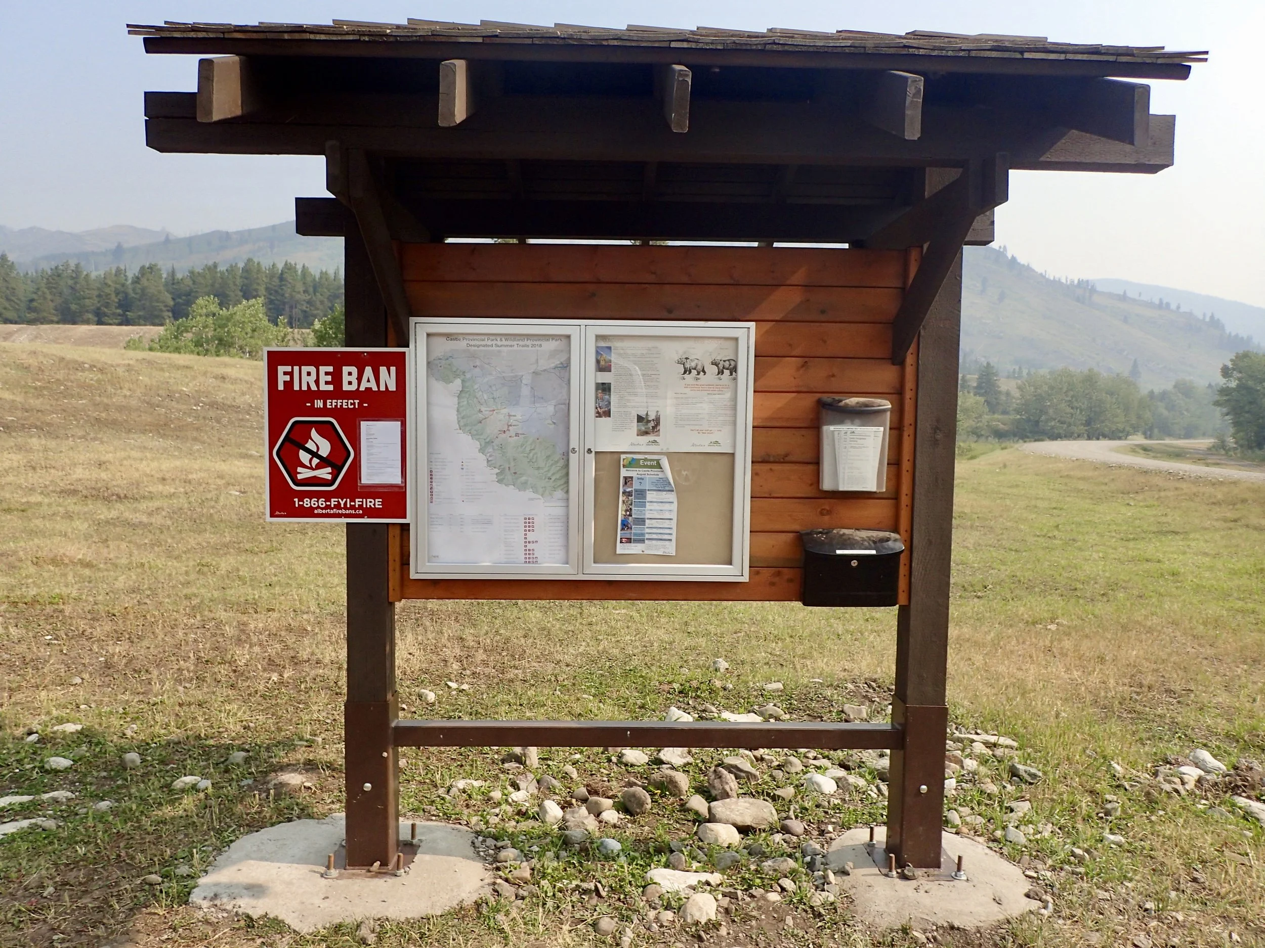 a trail map and fire ban sign on a grassy knoll