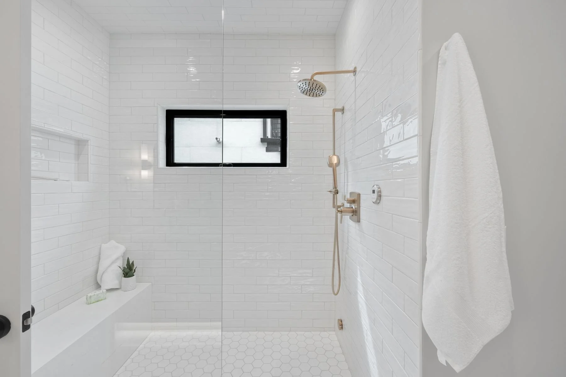 Modern white shower with a window, two showerheads and a towel hanging on the wall.