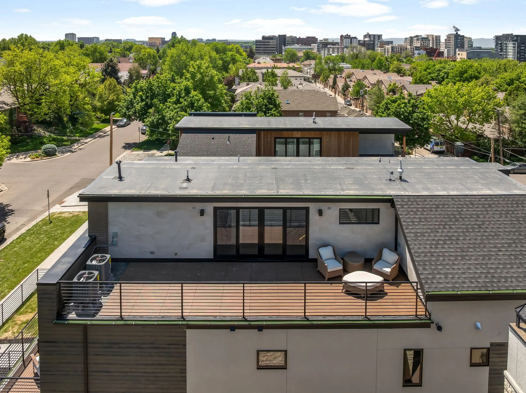 A rooftop terrace with outdoor furniture and a view of a residential neighborhood and cityscape in the distance.