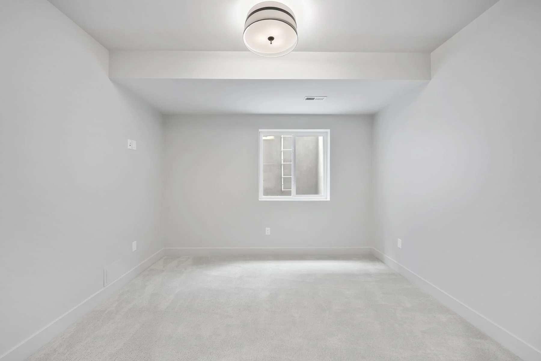 Empty finished room with white walls, a small window, beige carpet, ceiling light fixture, and outlets.