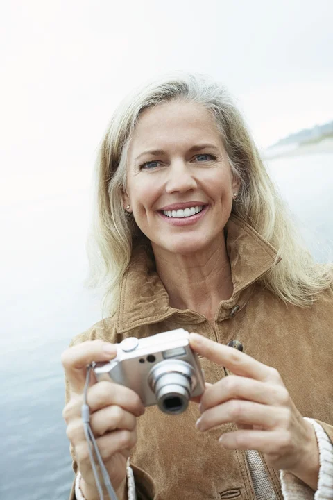 Attractive older woman holding camera smiling with dental implant